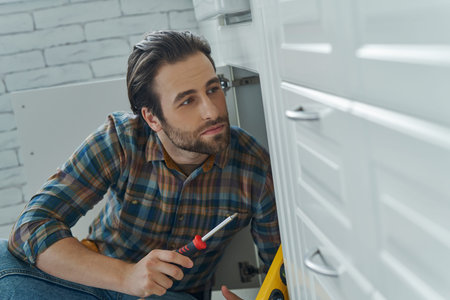 Confident young man repairing furniture at the domestic kitchenの写真素材