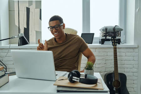 Cheerful young African man gesturing while having web conference in officeの写真素材
