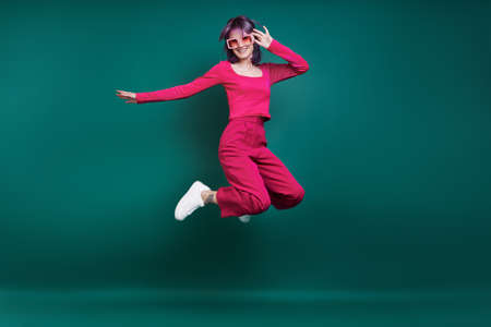 Cheerful young woman jumping against green backgroundの写真素材
