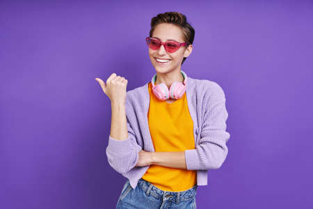 Cheerful young woman pointing away while standing against purple backgroundの写真素材