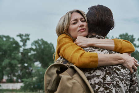 Depressed woman hugging her husband before leaving on warの写真素材