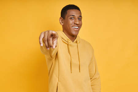Happy African man pointing camera while standing against yellow backgroundの写真素材