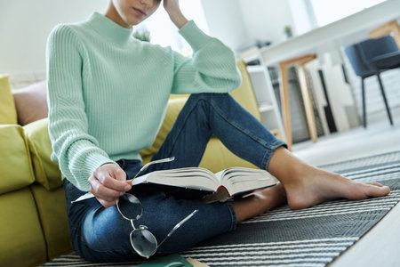 Close-up of tired woman holding book while sitting on the floor at home