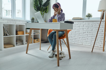 Confident young woman in headphones using laptop while sitting at her working place