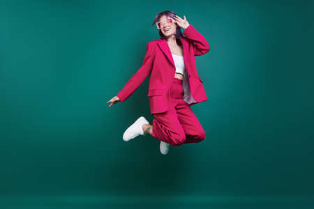 Funky young woman jumping against green backgroundの写真素材