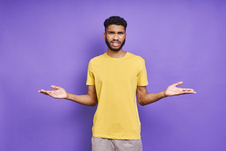 Frustrated African man gesturing while standing against purple background