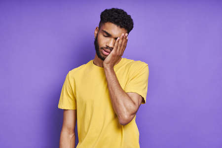 Depressed African man touching face while standing against purple backgroundの写真素材