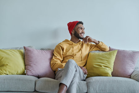 Handsome African man looking thoughtful while sitting on the couch
