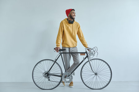 Happy young African man standing near his bicycle against the wall