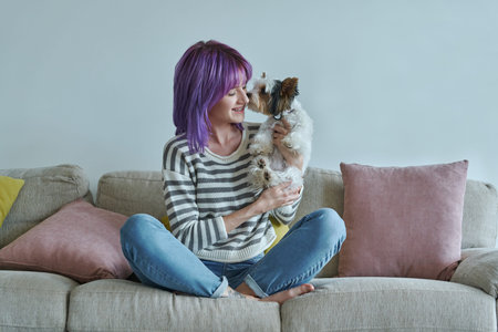 Cheerful teenage girl carrying her little dog while relaxing on the couch at home