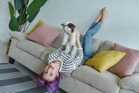 Playful teenage girl carrying her little dog while relaxing on the couch at home