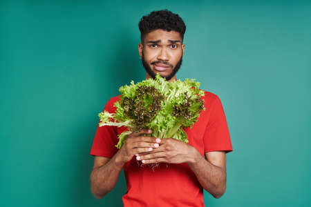 Frustrated African man holding a bunch of lettuce against green backgroundの写真素材