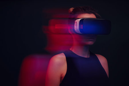 Confident young woman wearing virtual reality glasses against dark background