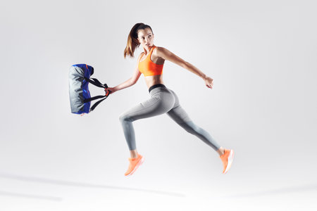 Full length of confident young woman carrying a bag and jumping against white background