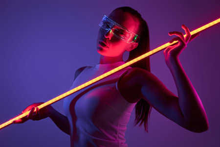 Attractive woman in futuristic glasses holding LED lamp against dark background