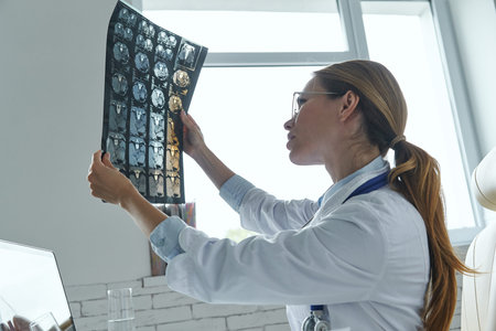 Female doctor examining medical X-ray while sitting at the officeの写真素材