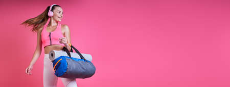Happy young woman in sports clothing carrying a bag against pink backgroundの写真素材