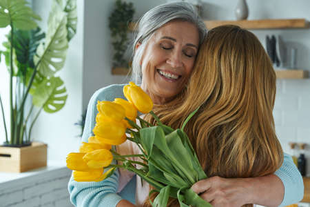 Joyful senior woman embracing her daughter and holding a bunch of yellow tulipsの写真素材