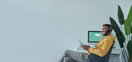 Dreamful African man holding digital tablet and smiling while sitting at his working placeの写真素材