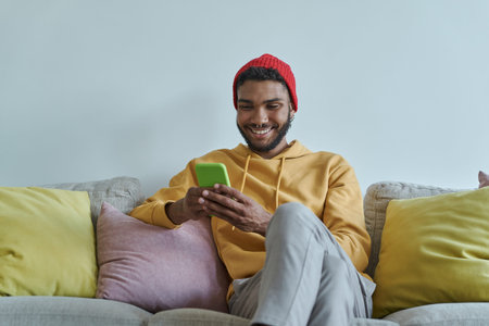 Cheerful young African man using smart phone while sitting on the couchの写真素材