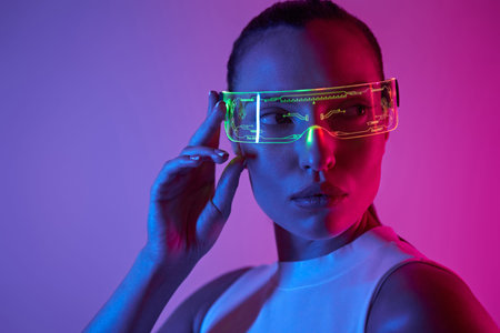 Beautiful young woman adjusting futuristic glasses against dark background