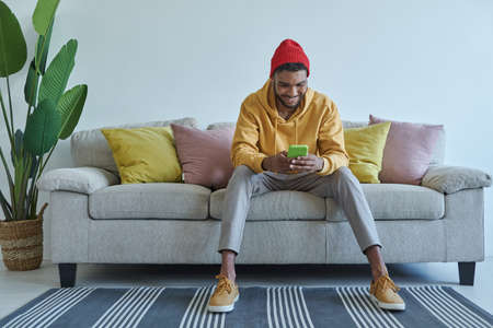 Handsome young African man using smart phone while sitting on the couchの写真素材