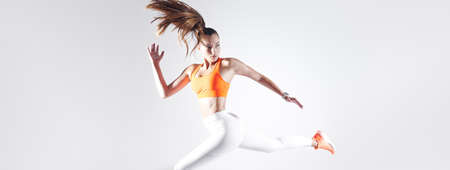Confident young woman in sports clothing running against white backgroundの写真素材