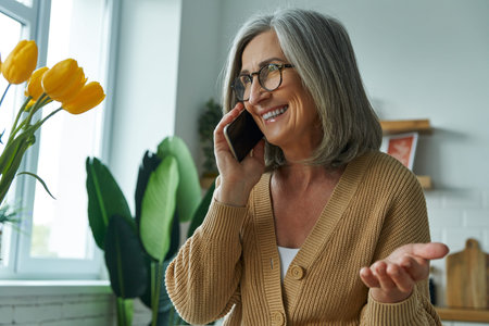 Happy senior woman talking on mobile phone and gesturing while relaxing at home