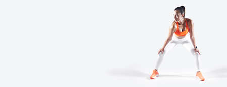 Confident young woman leaning on knees while standing against white backgroundの写真素材