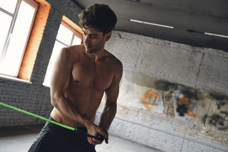 Handsome young man exercising with elastic resistance band in gym