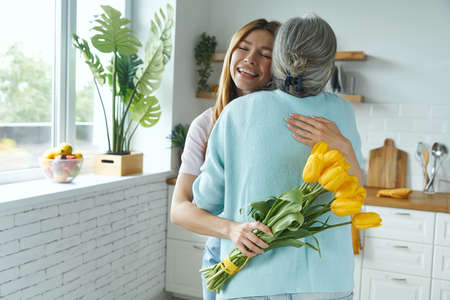 Happy young woman embracing her senior mother and holding a bunch of yellow tulipsの写真素材