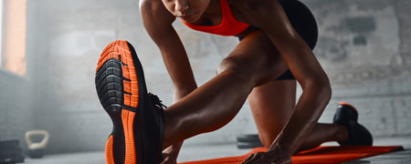 Close-up of young African woman doing stretching exercises in gym