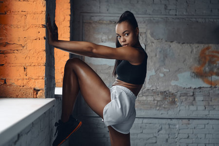 Confident African woman in sports clothing doing stretching exercises near the window in gym