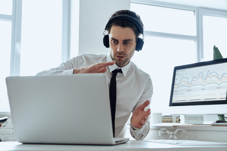 Concentrated young man in headphones gesturing while having web conference in office