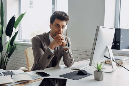 Confident young man in formalwear looking at camera while sitting in officeの写真素材