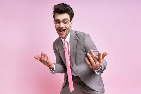 Happy young man in full suit gesturing while standing against pink backgroundの写真素材