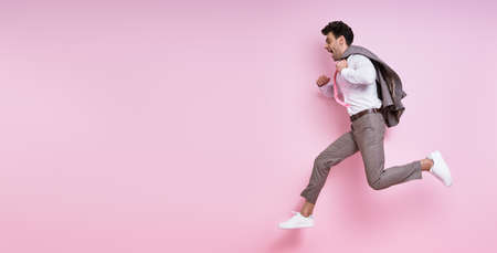 Excited man in shirt and tie carrying jacket on shoulder while jumping against pink backgroundの写真素材