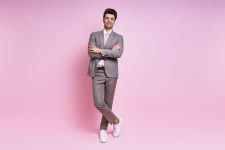 Handsome young man in full suit smiling while standing against pink backgroundの写真素材