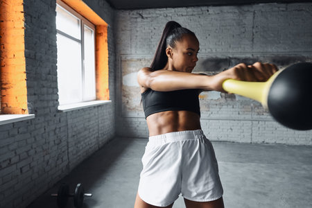 Confident young African woman exercising with kettlebell in gym