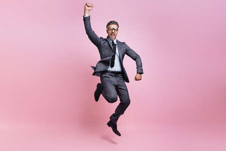 Excited mature man in full suit jumping and gesturing against pink backgroundの写真素材