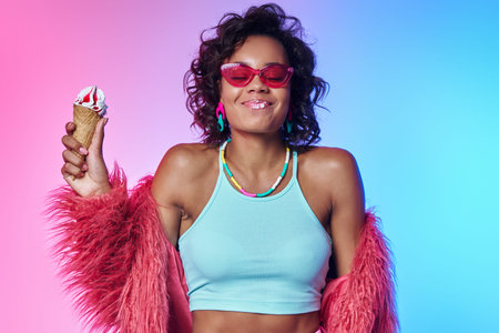 Joyful African woman in fluffy jacket eating ice cream and smiling against colorful background