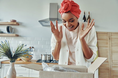 Surprised African woman looking at the opened box and gesturing while standing at kitchen