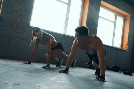 Young fit couple looking at each other and smiling while exercising in gym togetherの写真素材