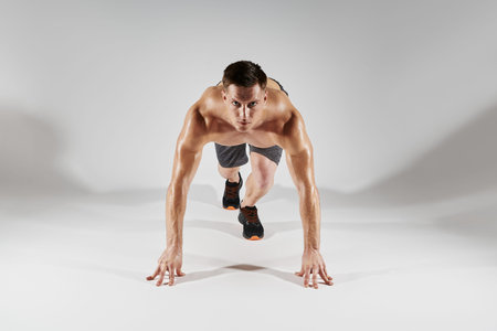 Confident fit man preparing to run while standing in starting position against white background