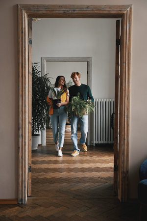Happy young couple holding houseplants while walking by their new apartment togetherの写真素材
