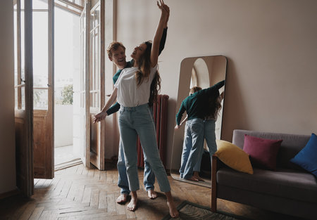 Playful young couple holding hands while relaxing at home togetherの写真素材