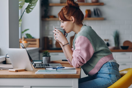 Beautiful woman drinking coffee while working from home at the domestic kitchenの写真素材