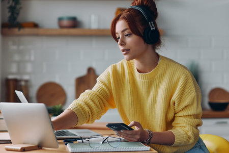 Confident young woman in headphones using technologies while sitting at the kitchen counterの写真素材