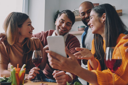 Group of young people looking at smart phone and smiling while enjoying time together