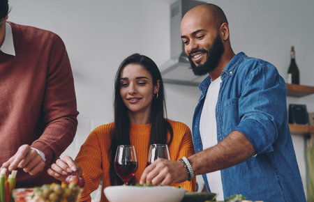 Happy young people enjoying food and drinks while having dinner at home together
